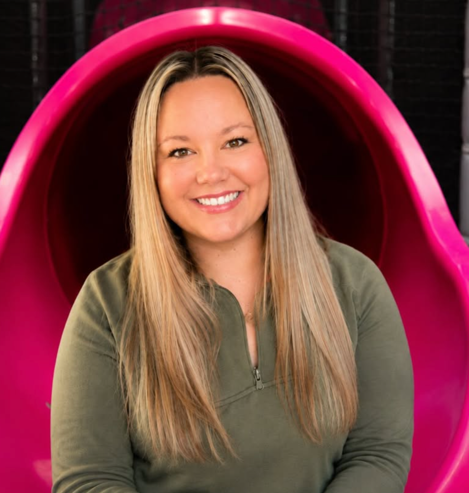 Chelsea Dickens Parks, owner of Plum Krazy Play, smiling inside a pink slide tunnel