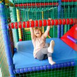 A little girl sitting on top of a bed in a play area.