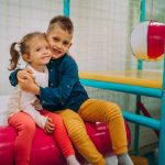 Two children sitting on a pink and blue ball.