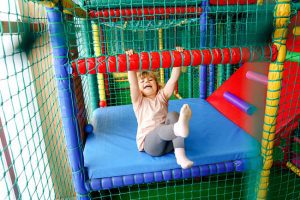 A little girl hanging from the bars of an indoor play area.