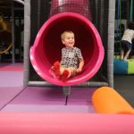 A little boy is sitting in the tunnel of an indoor play area.